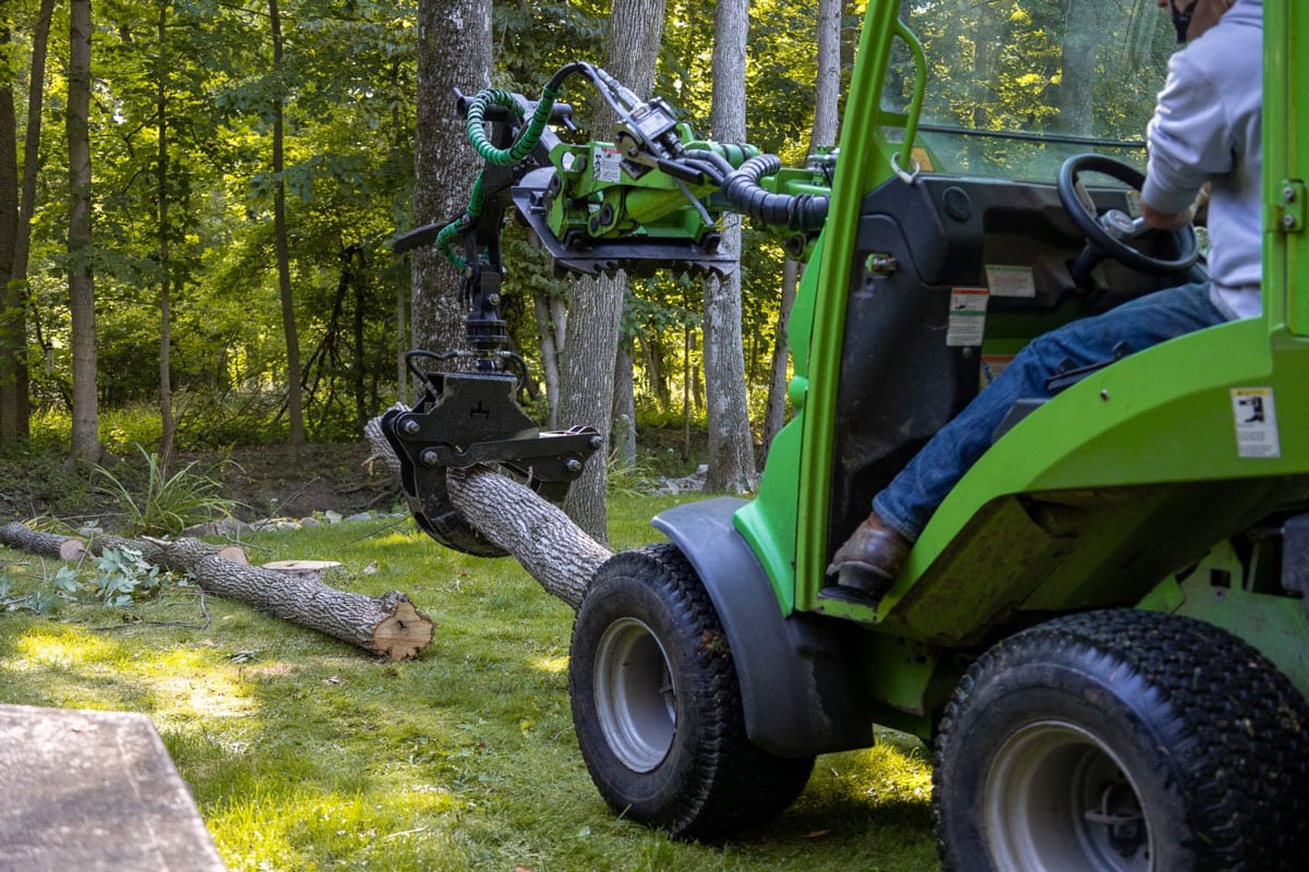 Man in a green tractor collecting tree debris. The tractor has a large black wheel.