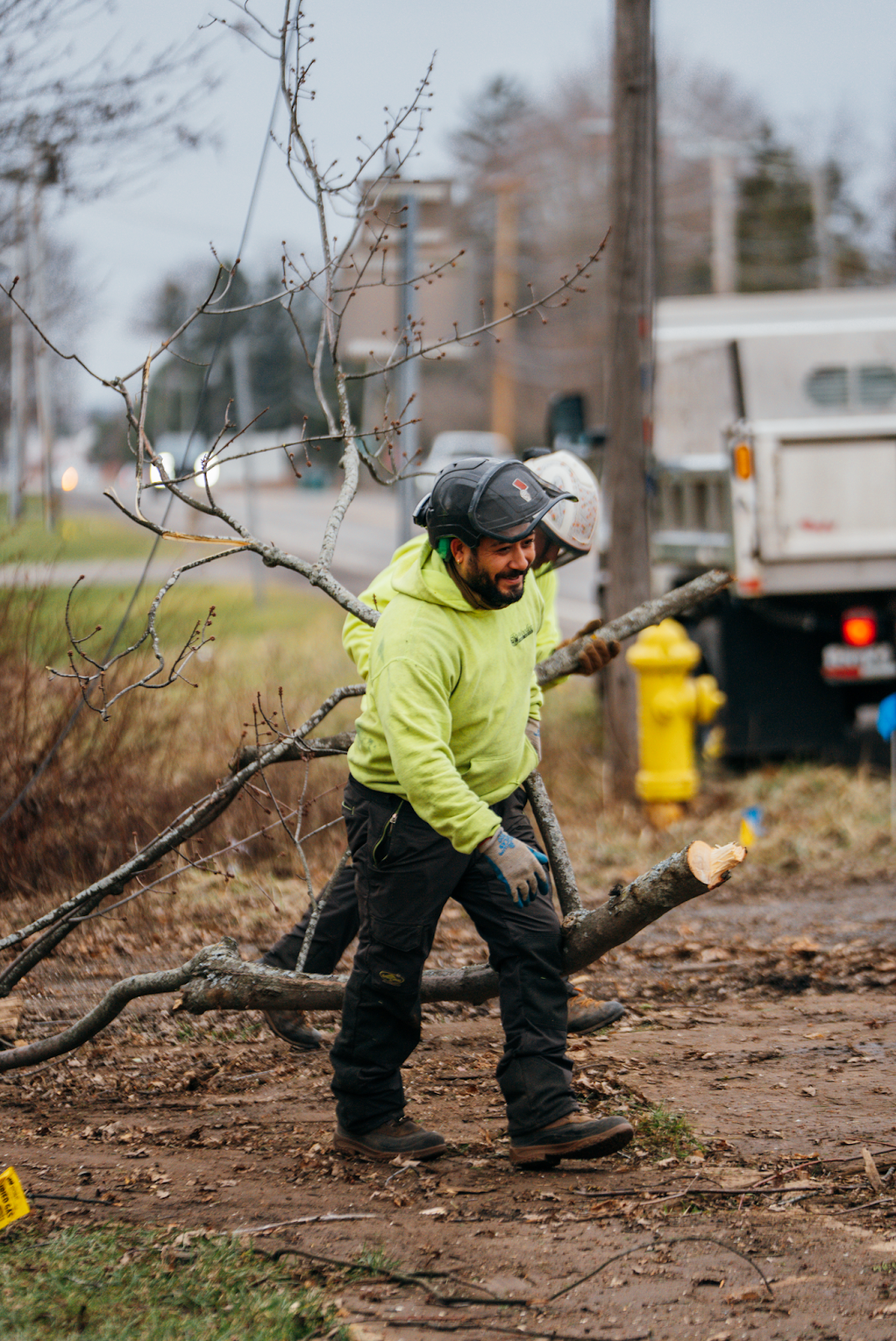 Man in neon green hoodie and safety gear carrying branch. He appears to be a tree worker.