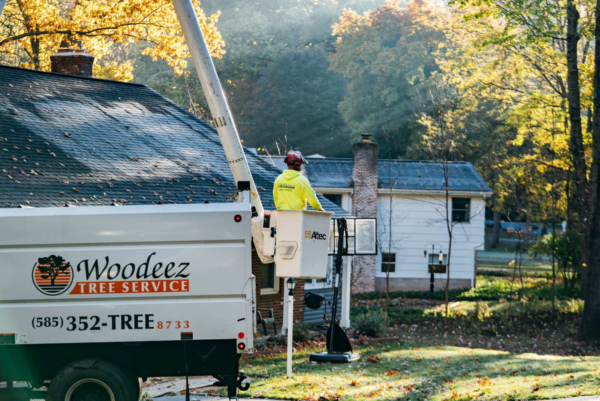 A worker in a bucket truck trimming trees. Professional tree care service.