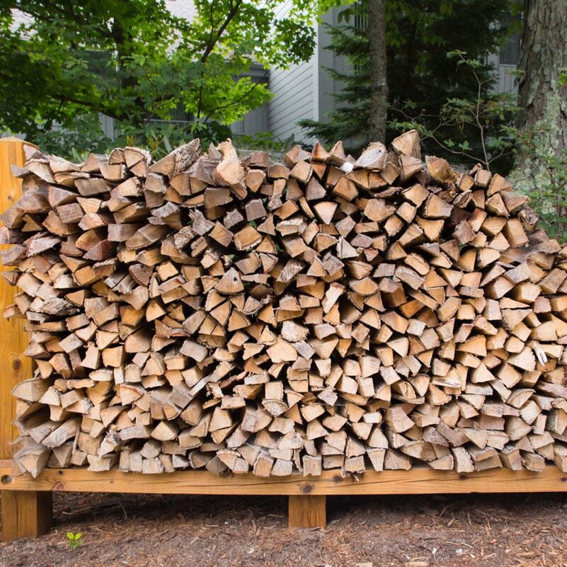 A large pile of chopped firewood on a rack. The wood is neatly arranged.